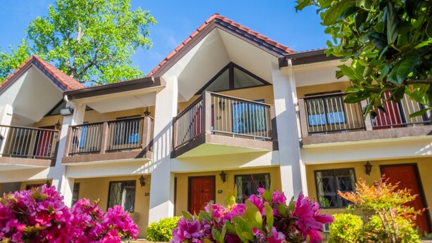 A multi-story hotel with balconies, a red-tiled roof, and a well-maintained garden with pink flowers. - Super 8 by Wyndham Downtown Gatlinburg at Convention Center (Gatlinburg)