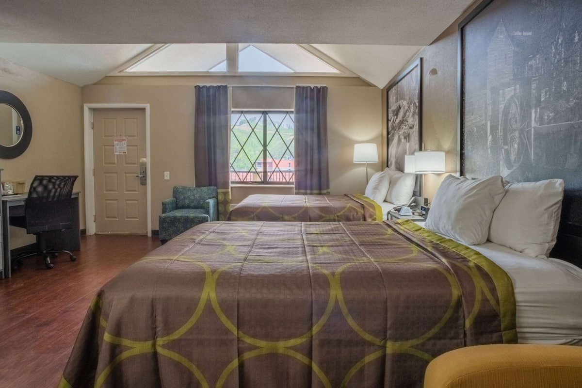 A hotel room with a large bed, a desk, a chair, and a window with curtains.