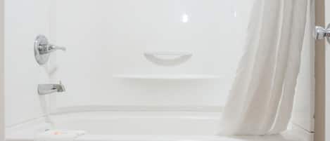 A modern bathroom with a white bathtub, a white toilet, and a wooden floor.