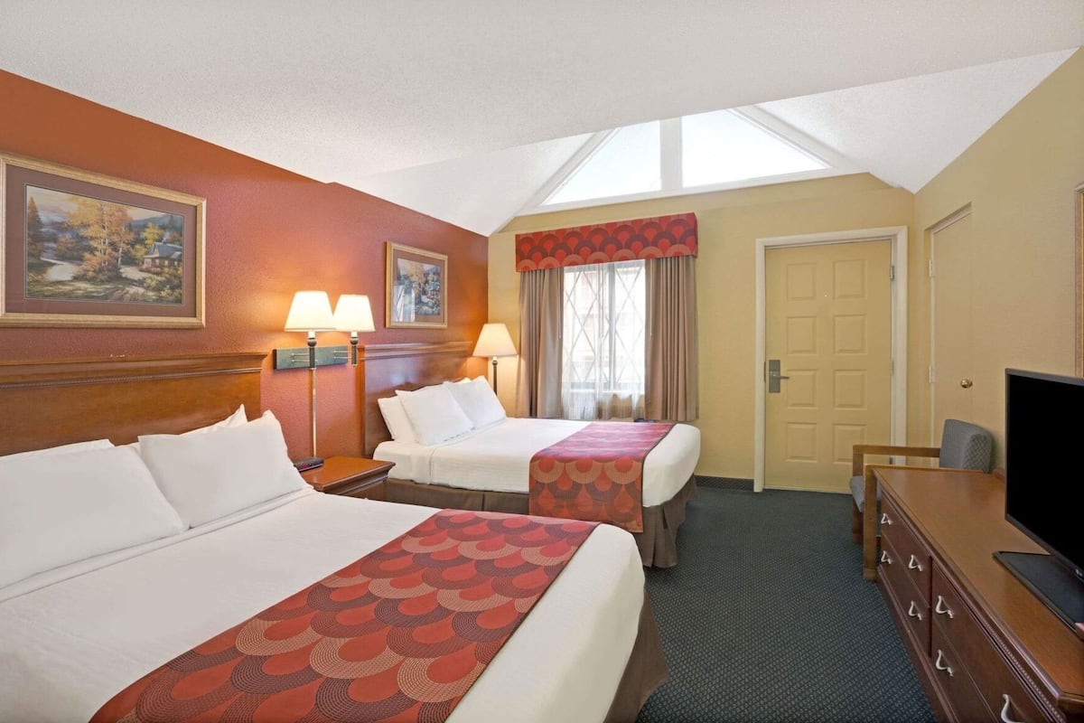 A hotel room with two beds, a desk, a television, and a window with curtains.