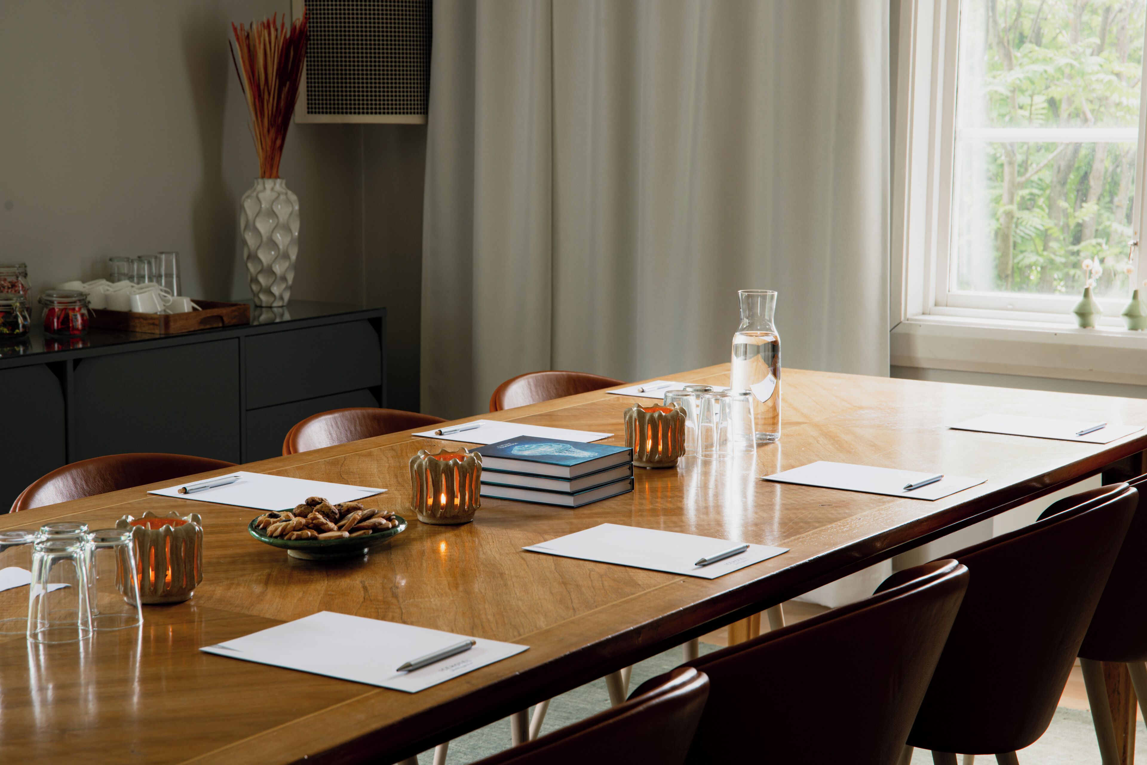 A conference table with chairs, a vase, a bowl of nuts, a book, and a water bottle.