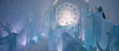 An ice hotel interior with a central dome and ice sculptures.