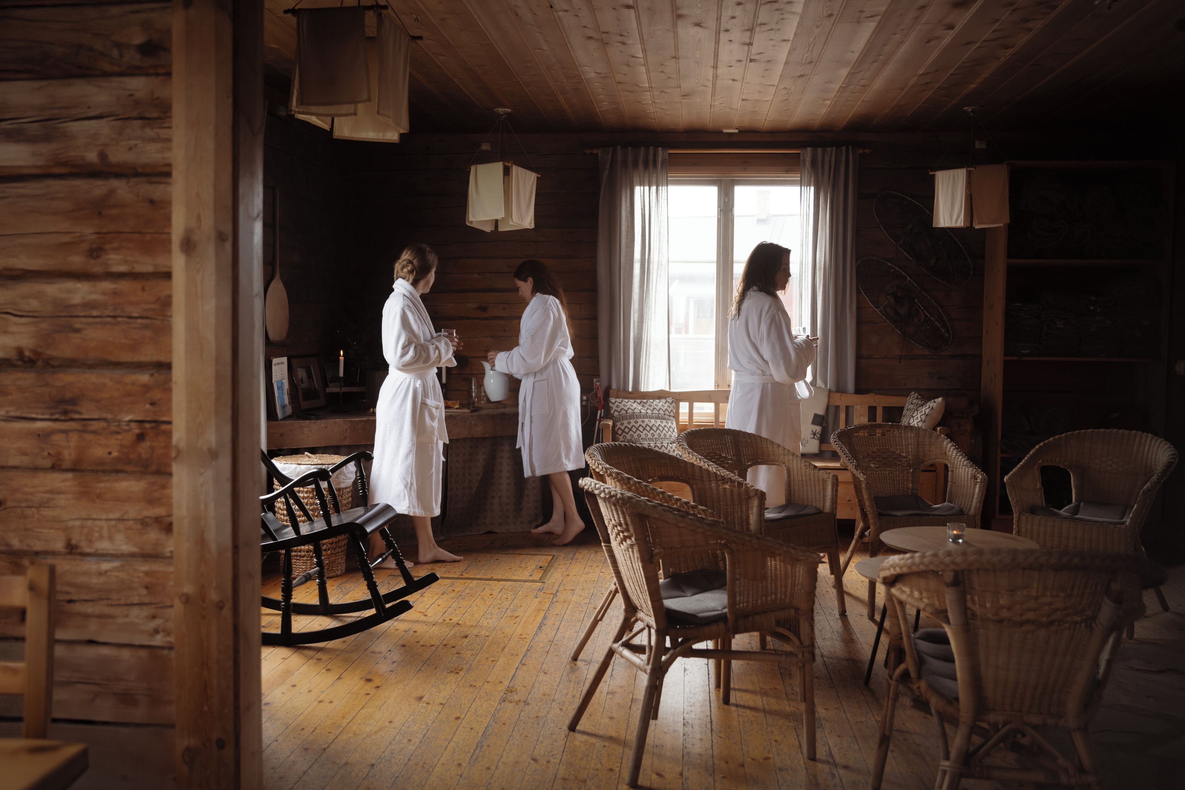 A rustic wooden cabin interior with wicker furniture, a rocking chair, and a dining table.