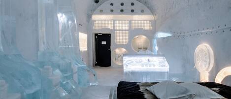 Una habitación de hotel de hielo con cama, escritorio y esculturas de hielo.