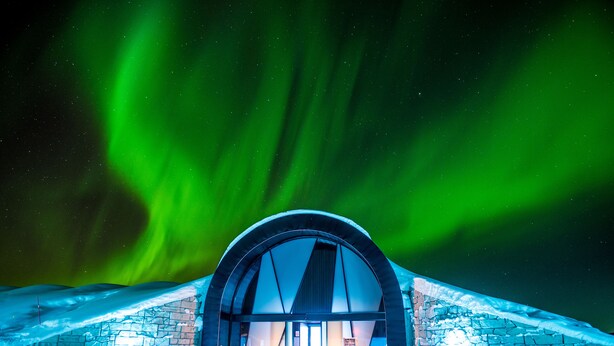A snow-covered building with a large arched entrance, under a night sky with green aurora borealis.