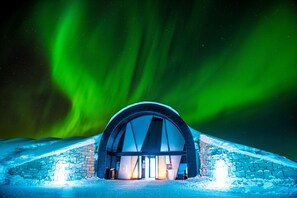 A snow-covered building with a large arched entrance, under a night sky with green aurora borealis. - Ice Hotel (Jukkasjärvi)