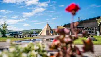 A reception building with a sign, a teepee, picnic tables, and a boat in the background.