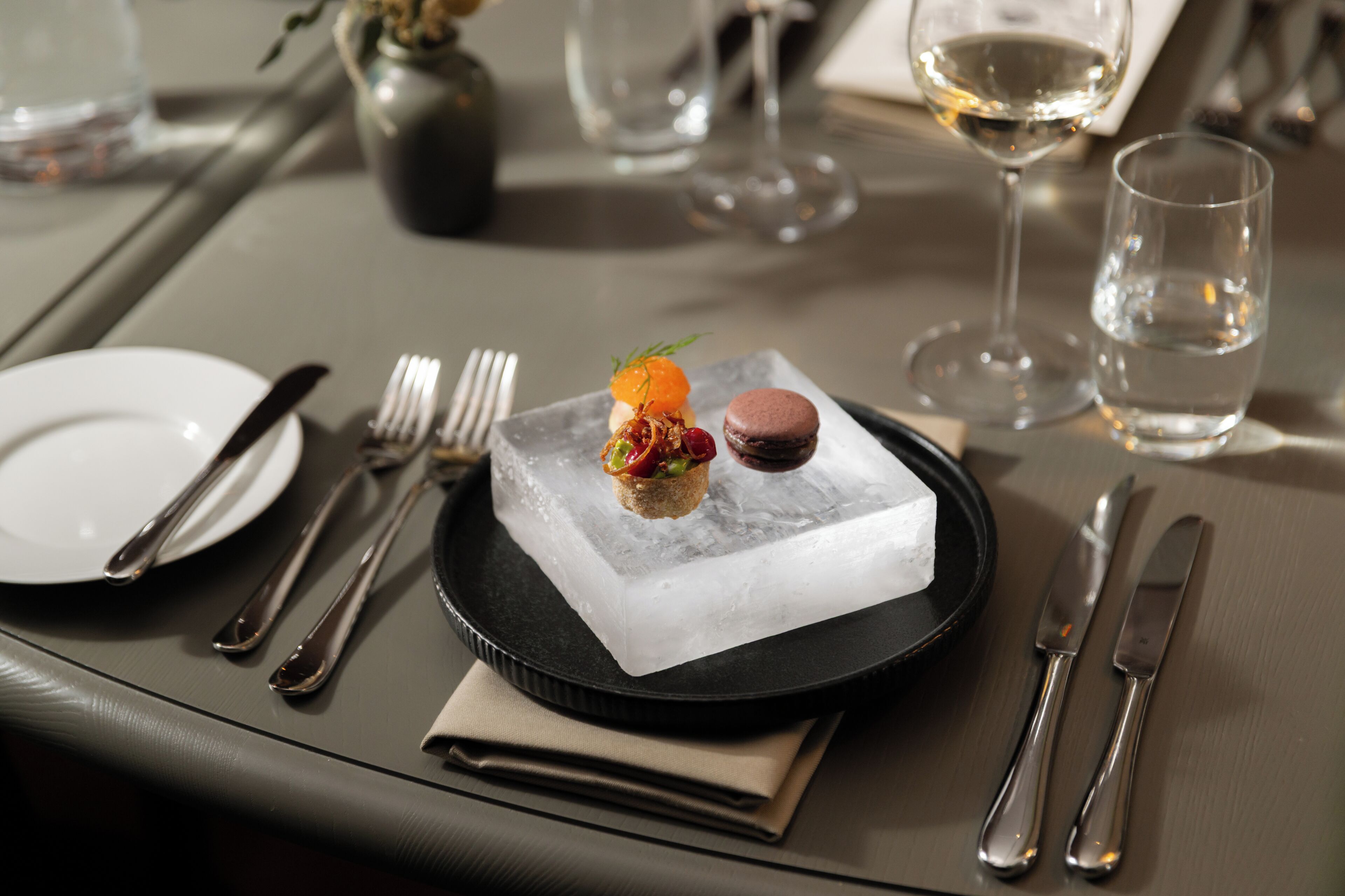 Een eettafel met een dessert op een zwart bord, bestek en een glas water.