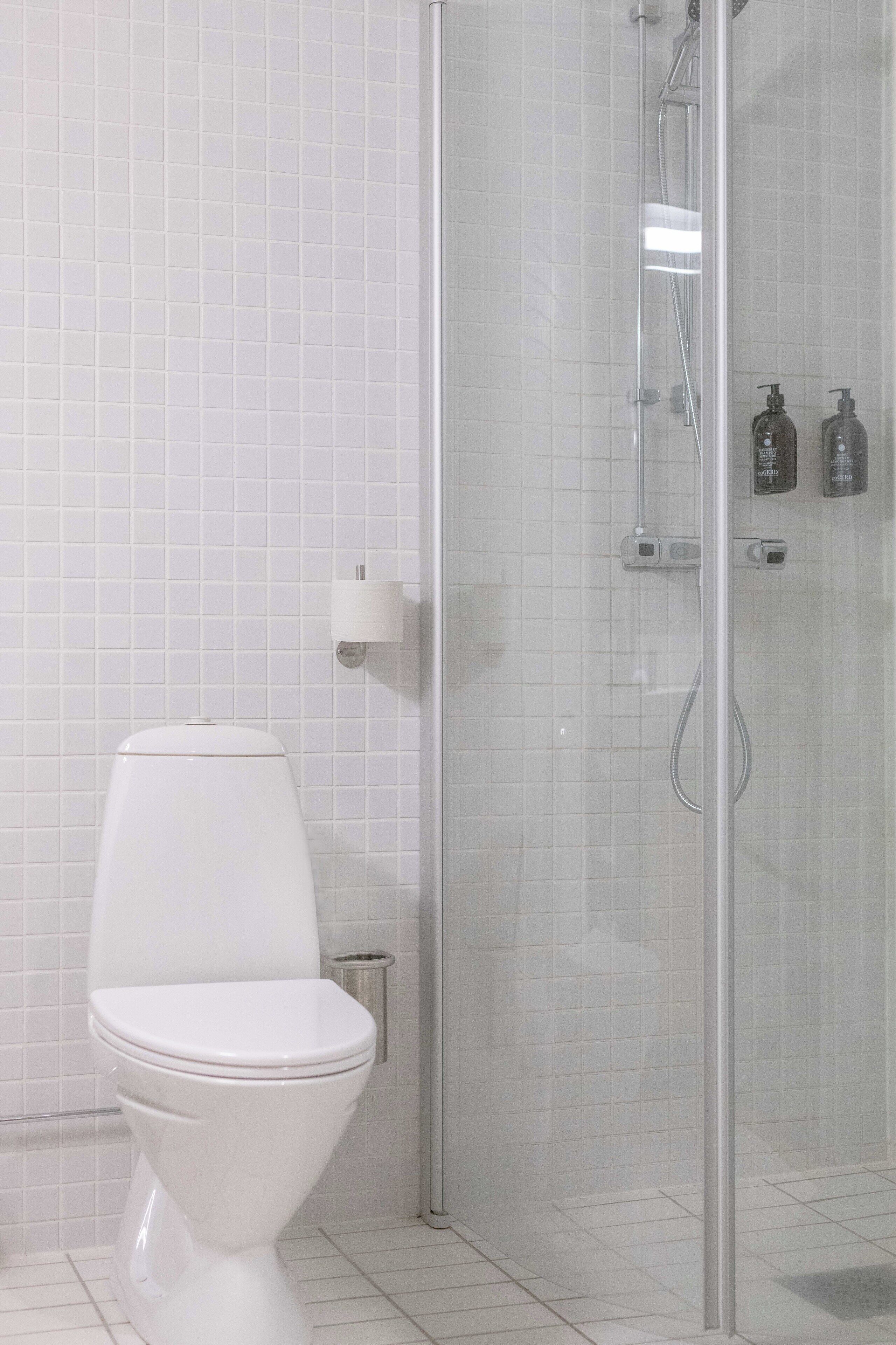 A modern bathroom with a toilet, a glass-enclosed shower, and white tiled walls.
