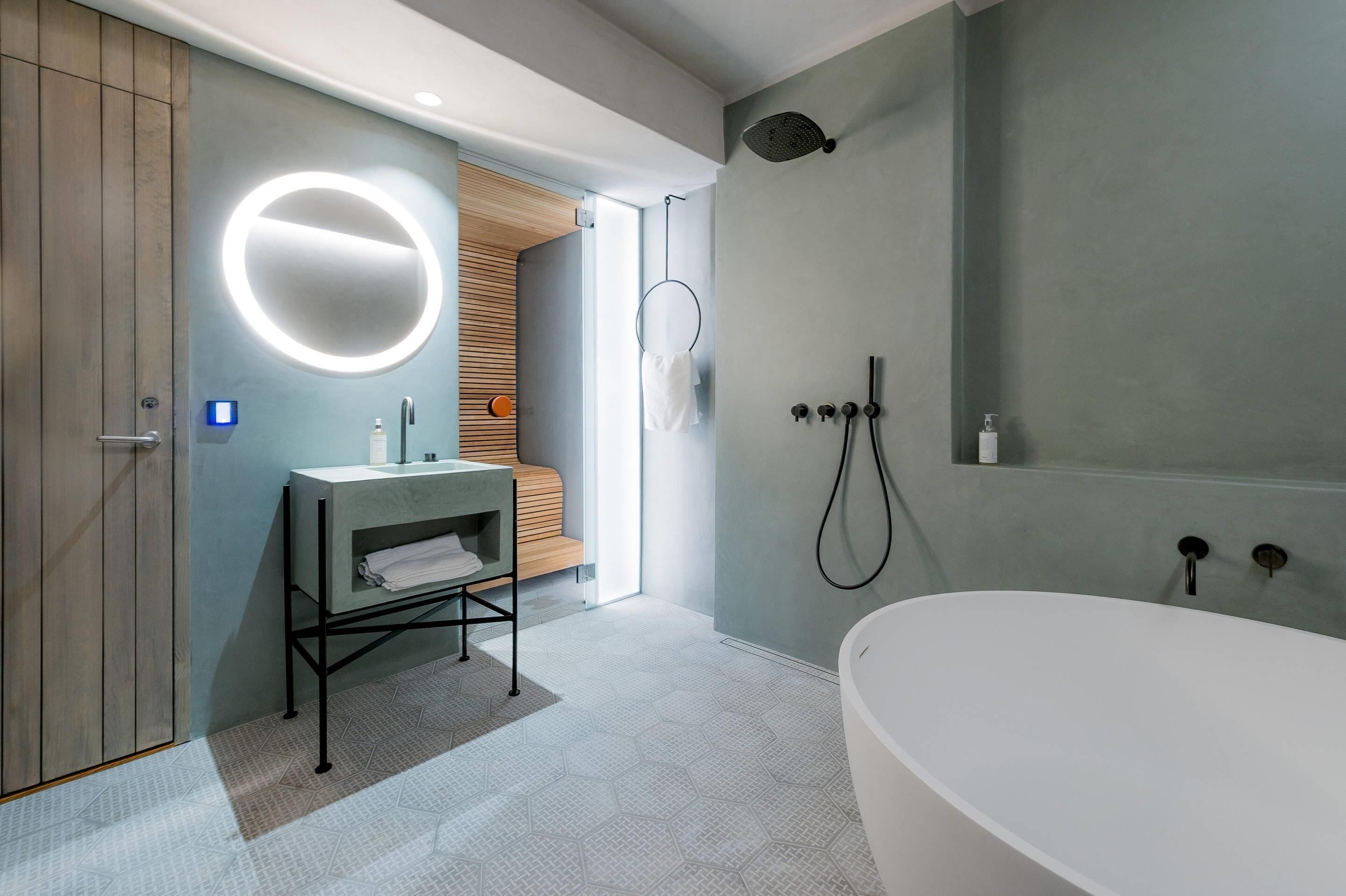 Une salle de bain moderne avec une baignoire sur pieds, un miroir rond avec éclairage intégré et un meuble-lavabo en bois.