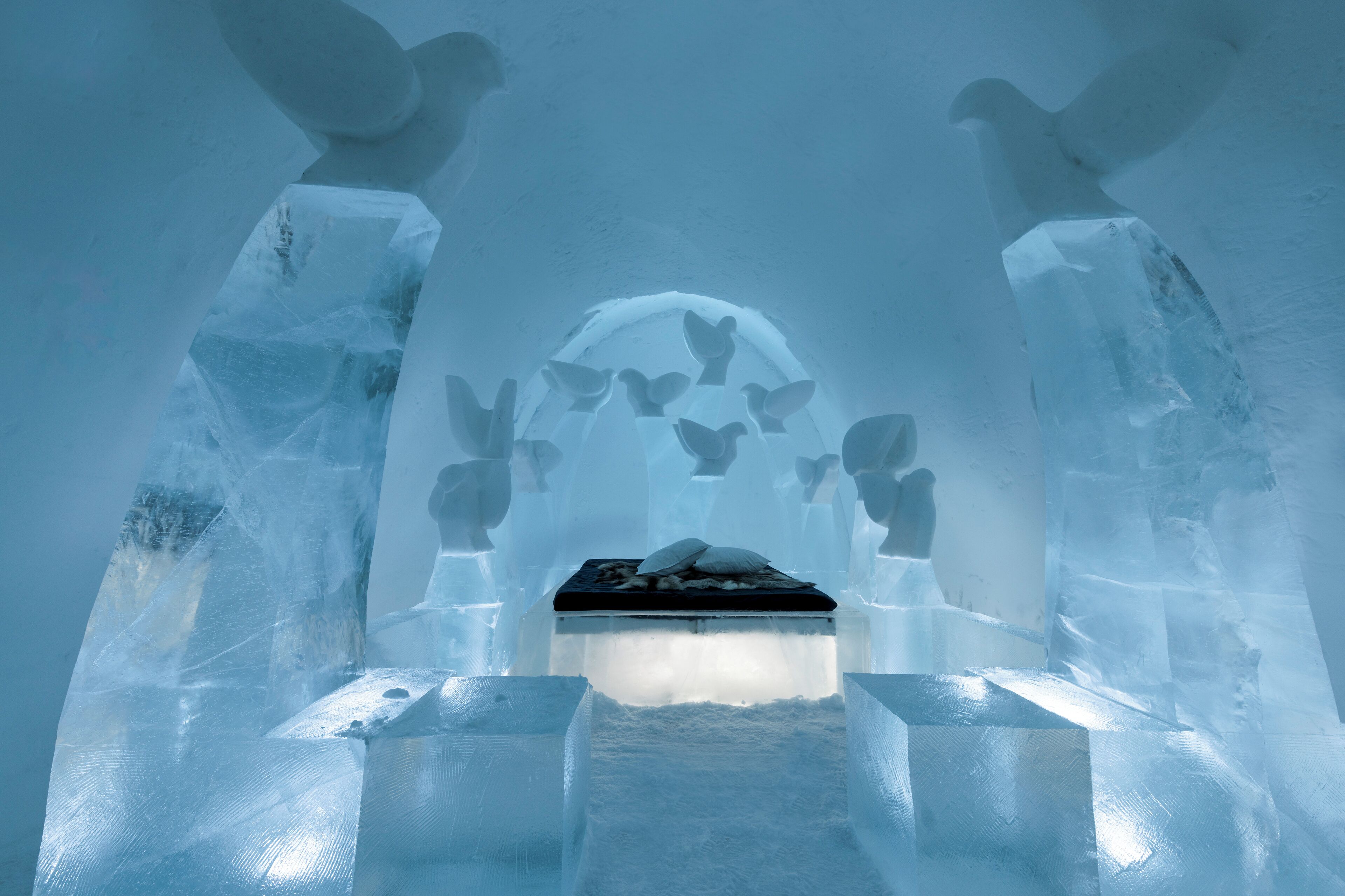 Interior de un hotel de hielo con una zona de estar central rodeada de paredes y bancos de hielo.