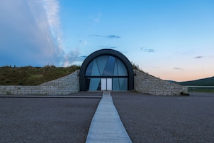 Un edificio moderno con una amplia entrada en arco, un camino de piedra que lo conduce y un cielo despejado al fondo.
