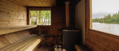 A cabin with a wooden interior, a sauna, a window overlooking a forested area, and a view of a river.
