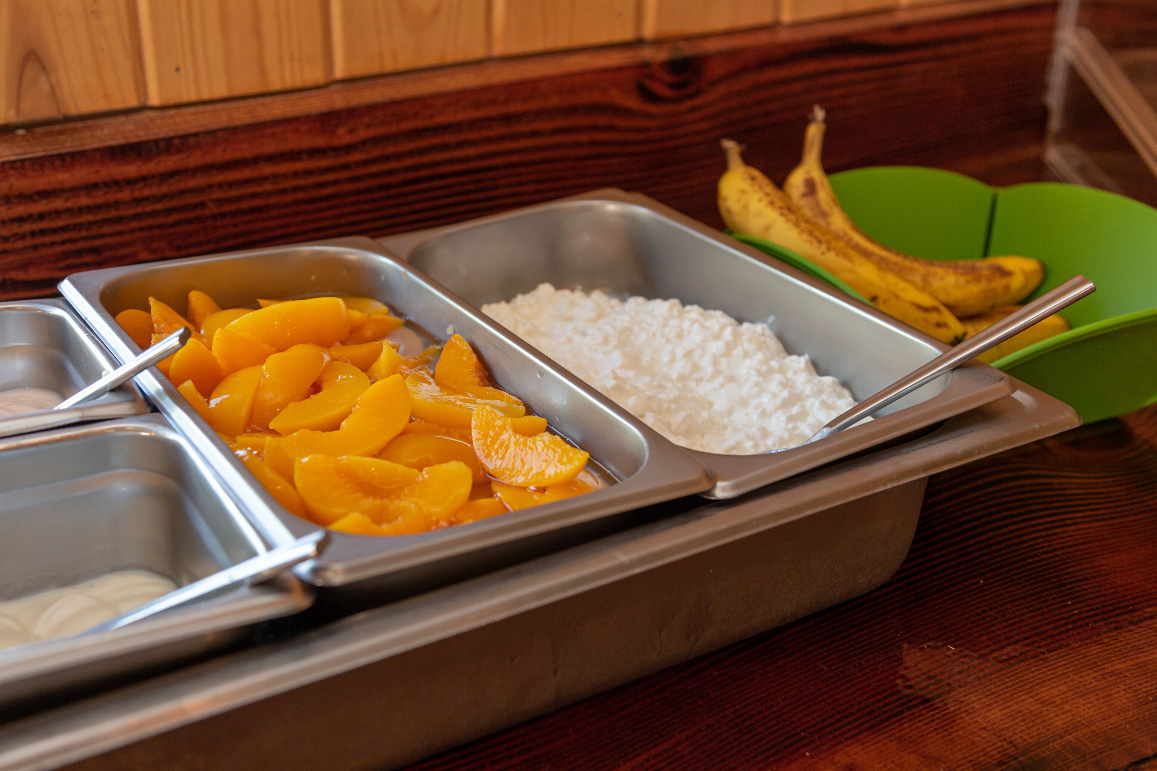 A buffet with three trays containing peaches, rice, and bananas.