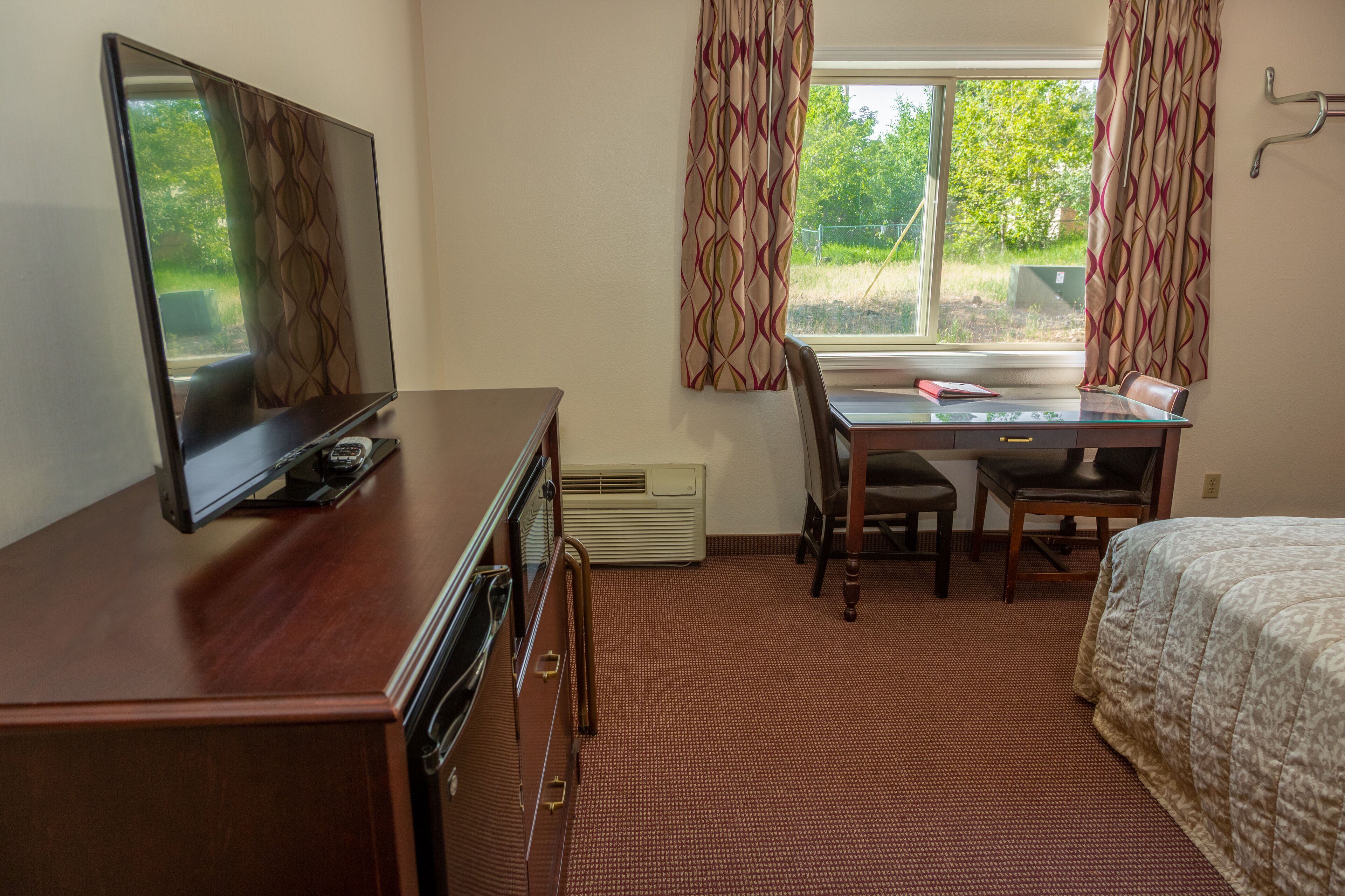 A hotel room with a bed, a desk with a chair, a television, and a window with curtains.
