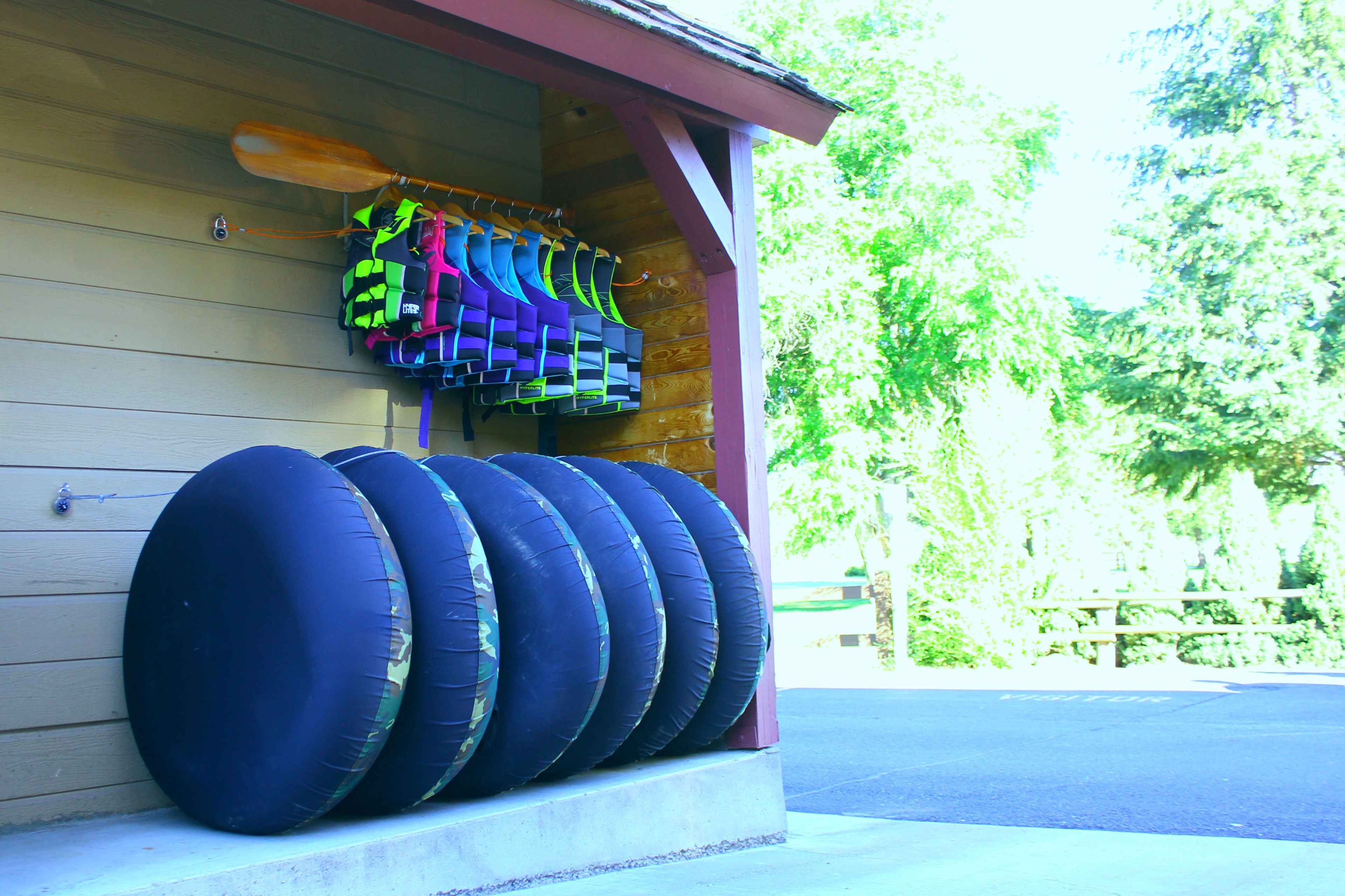 A row of blue tires against a wooden wall, with a paddleboard and life vests hanging above.