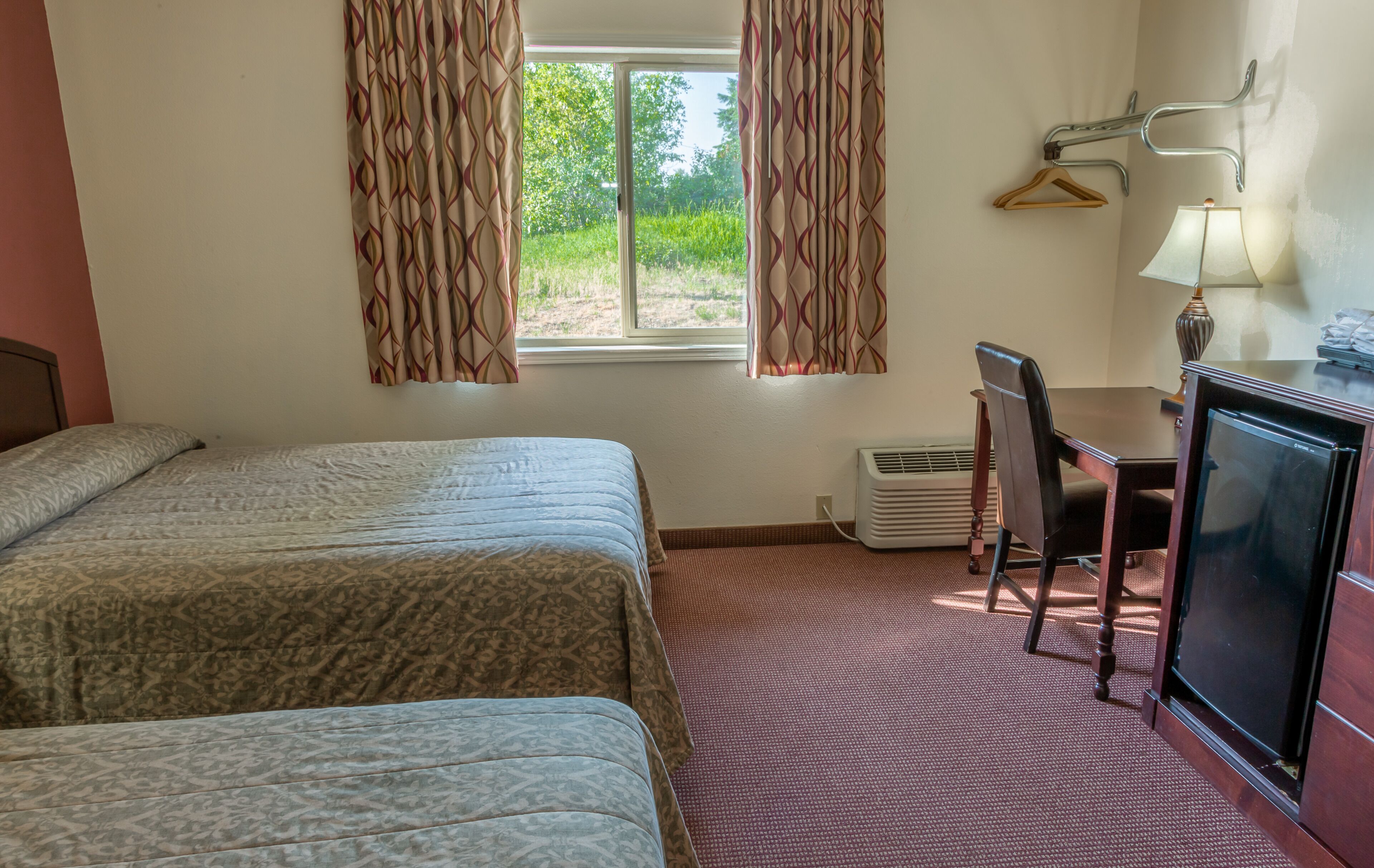 A hotel room with two beds, a desk, a chair, a TV, and a window with curtains.