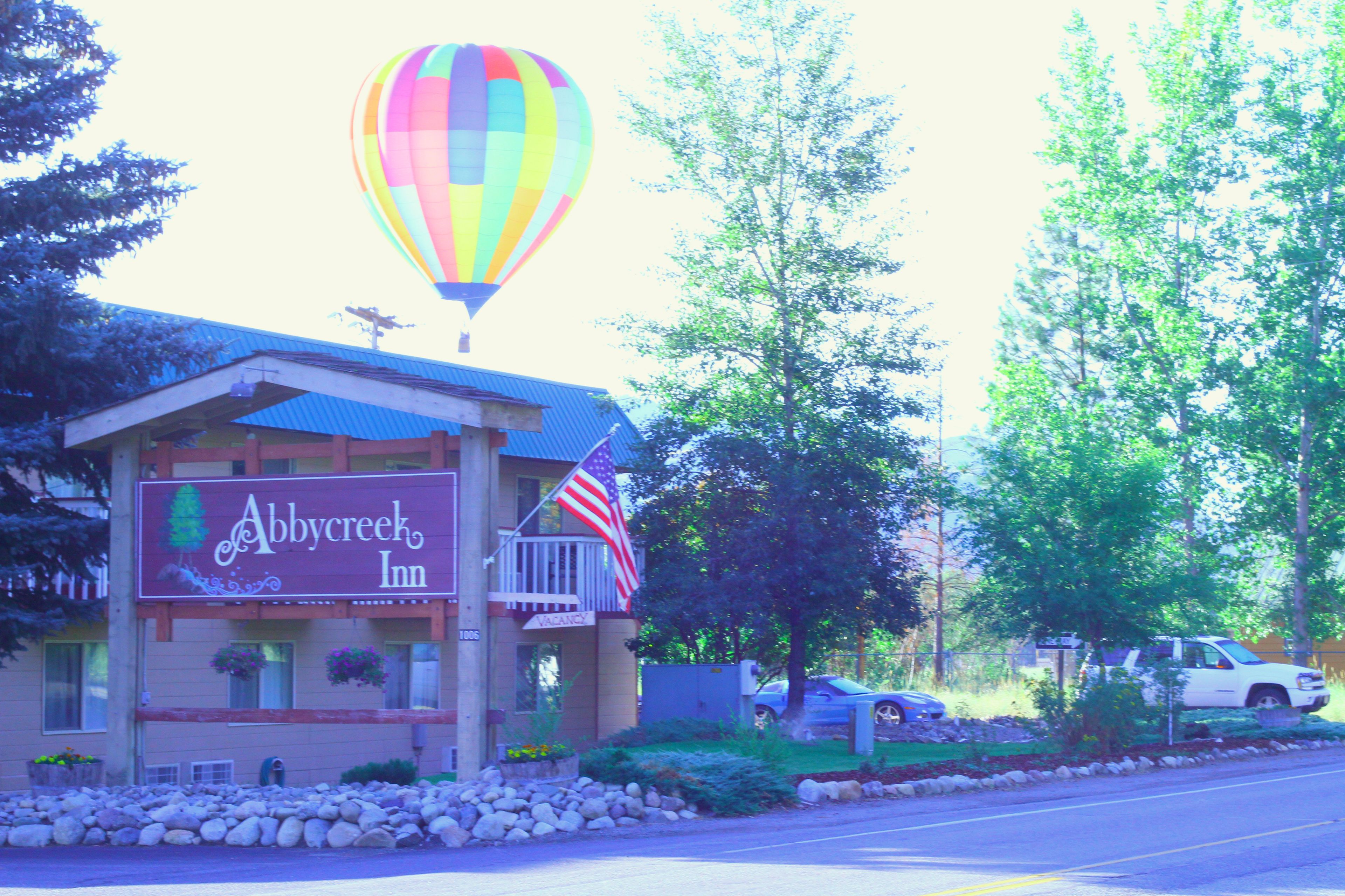Ein Motel mit einem bunten Heißluftballon im Hintergrund, einer amerikanischen Flagge und einem Schild, auf dem 'Abby Creek Inn' steht.