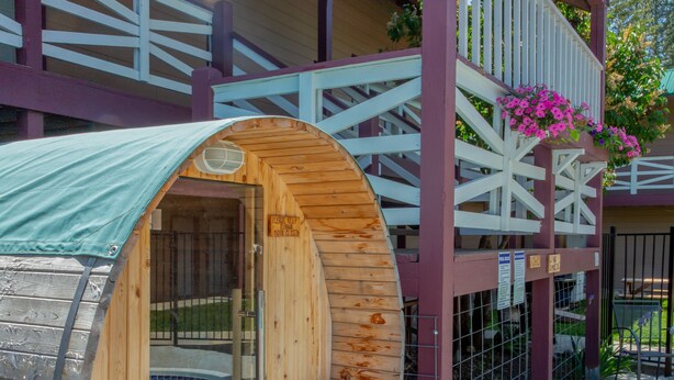 A wooden sauna with a curved roof, a bench inside, and a view of a building with a balcony and a fence.