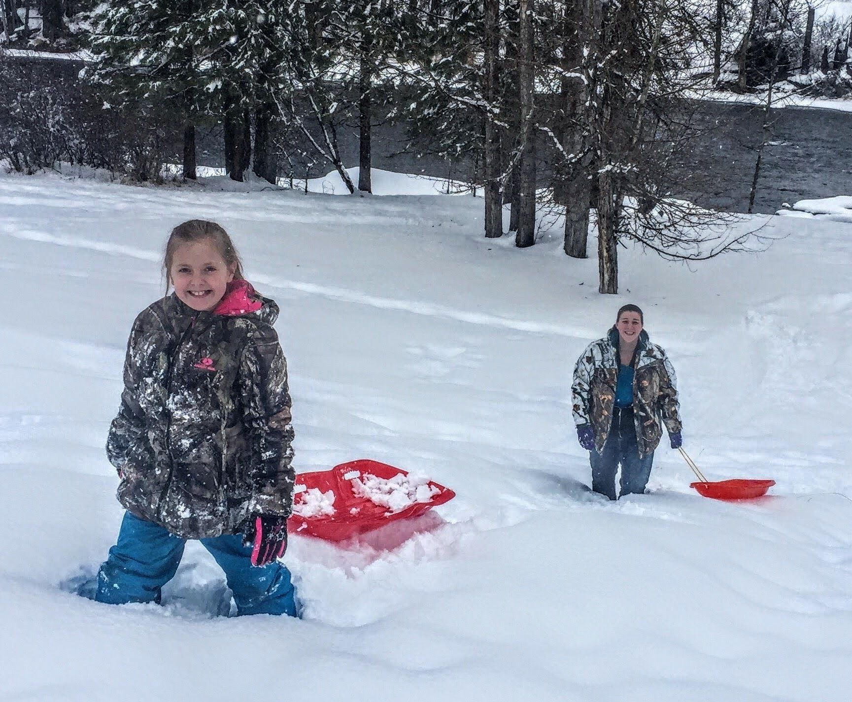 Two people in a snowy outdoor area with a red sled.