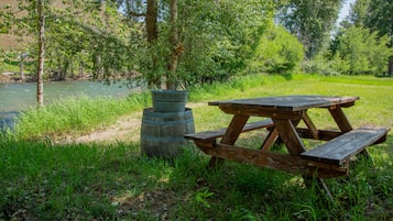 Una mesa de picnic y un barril con un cartel en un área verdejante cerca de un río.