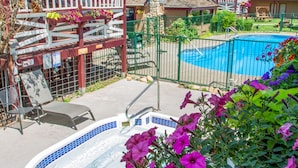 A pool area with a hot tub, surrounded by a wooden deck and a stone wall.