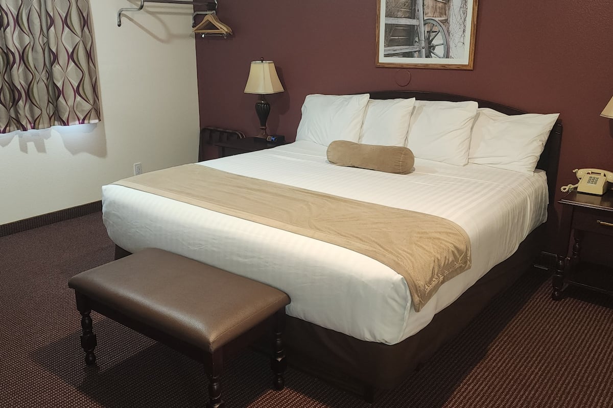 Une chambre d’hôtel avec un grand lit, une table de chevet avec une lampe, un téléphone et un banc.