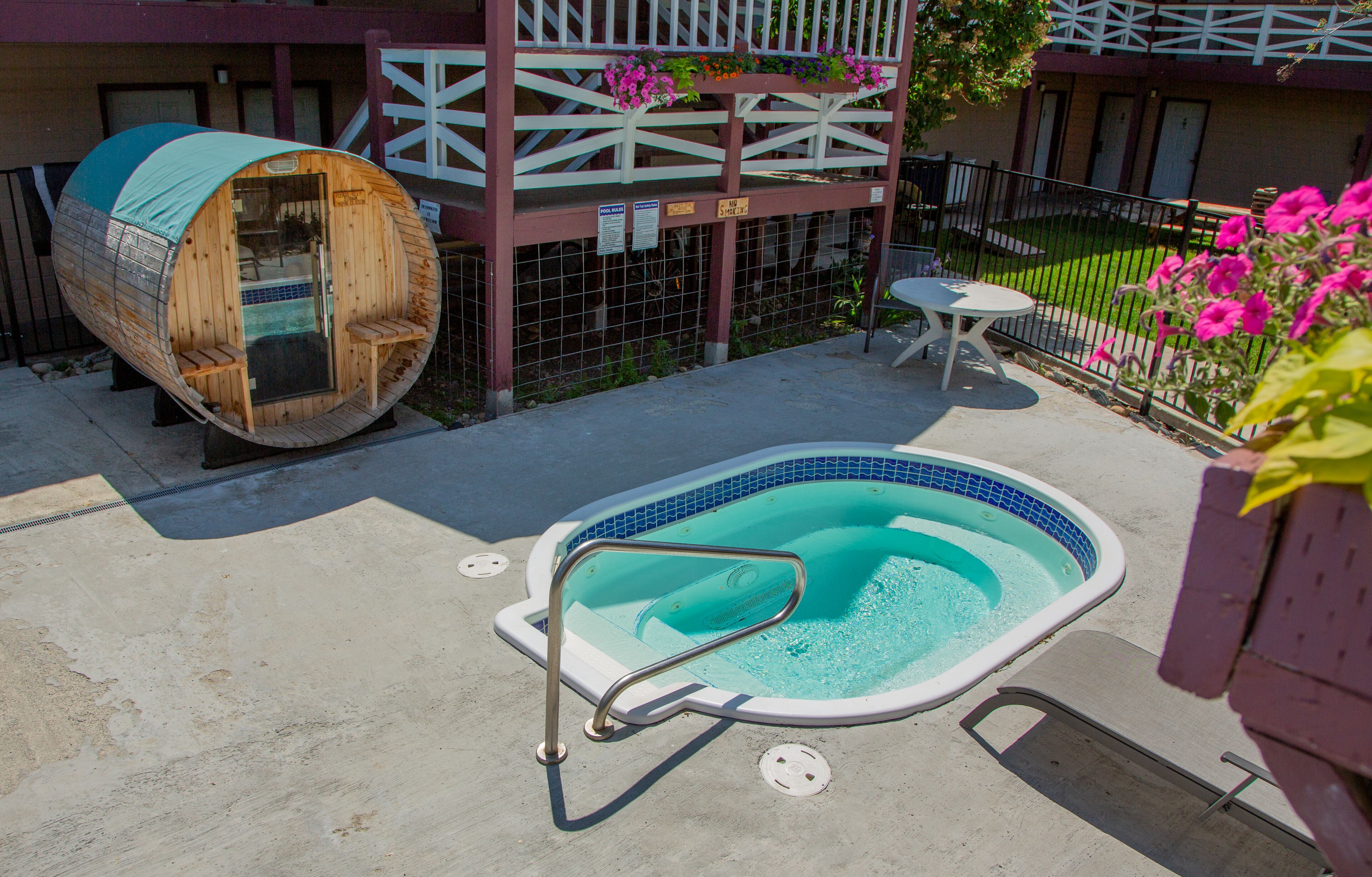 Un jacuzzi con una escalera metálica, un barril de madera y una pequeña mesa con sillas.