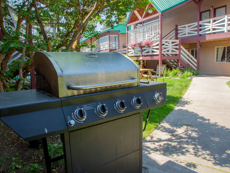 A barbecue grill with four burners, located in a courtyard with a building in the background.