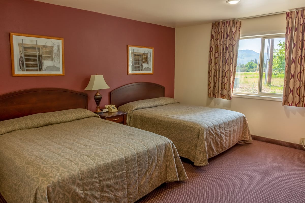 Une chambre d’hôtel avec deux lits, une table de chevet, une lampe et une fenêtre avec des rideaux.