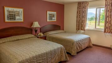 A hotel room with two beds, a nightstand, a lamp, and a window with curtains.