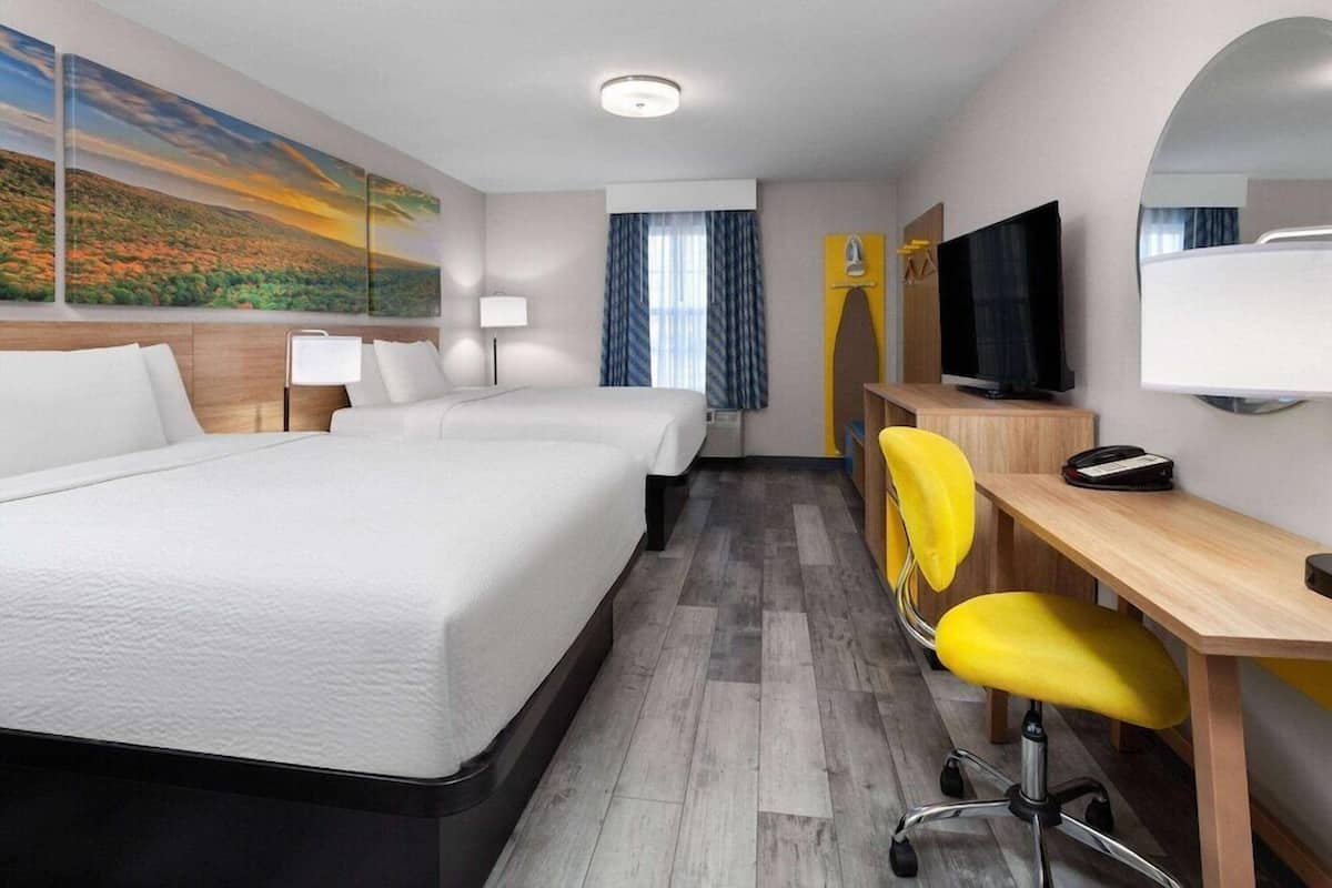 A hotel room with a bed, two bedside tables, a desk with a chair, a television, and a large window with curtains.
