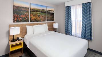 Una habitación de hotel con una cama grande, dos mesitas de noche con lámparas, una mesita con un teléfono y una ventana con cortinas azules.