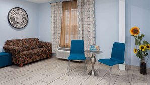 A living room with a sofa, two chairs, a small table, a clock, and a window with curtains. - Days Inn & Suites by Wyndham Sellersburg (Sellersburg)
