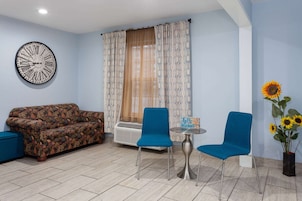 Una sala de estar con un sofá, dos sillones, una mesita, un reloj y una ventana con cortinas.