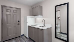 A compact kitchen with a refrigerator, sink, and cabinets. - Days Inn & Suites by Wyndham Sellersburg (Sellersburg)