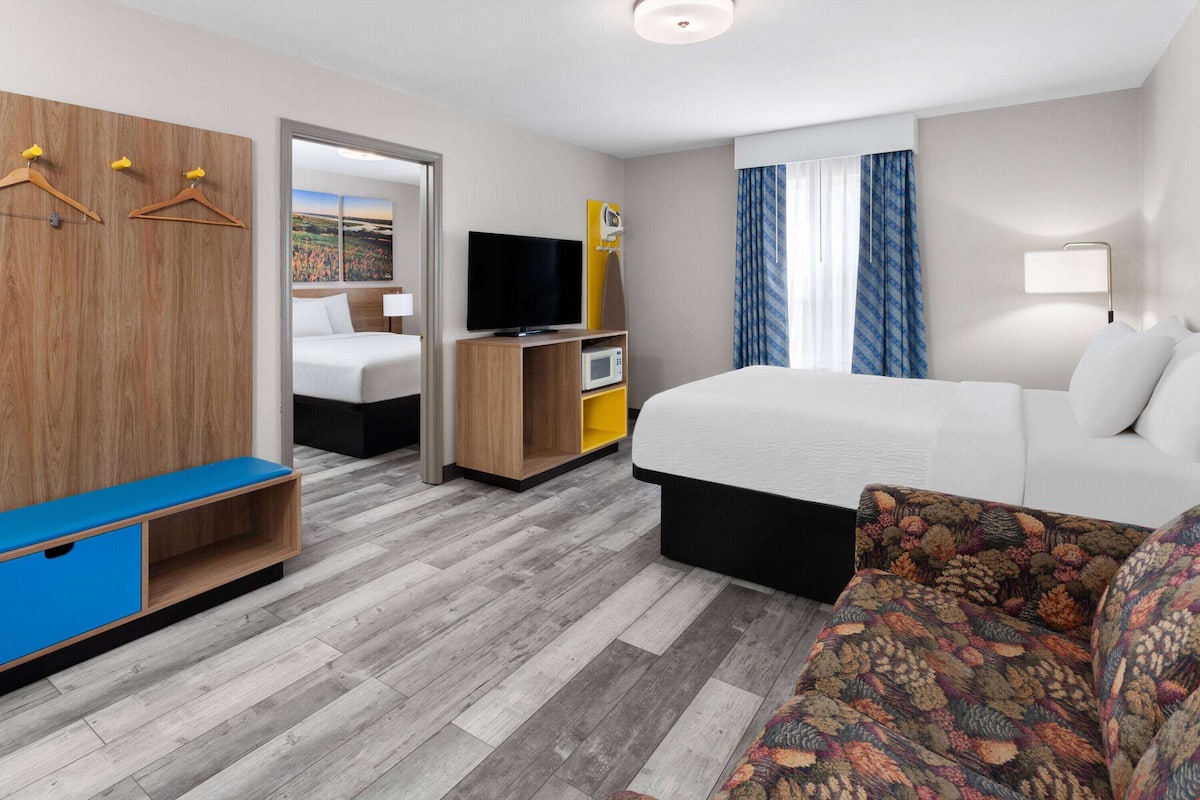 A hotel room with a bed, a TV, a wardrobe, a desk, and a window with curtains.