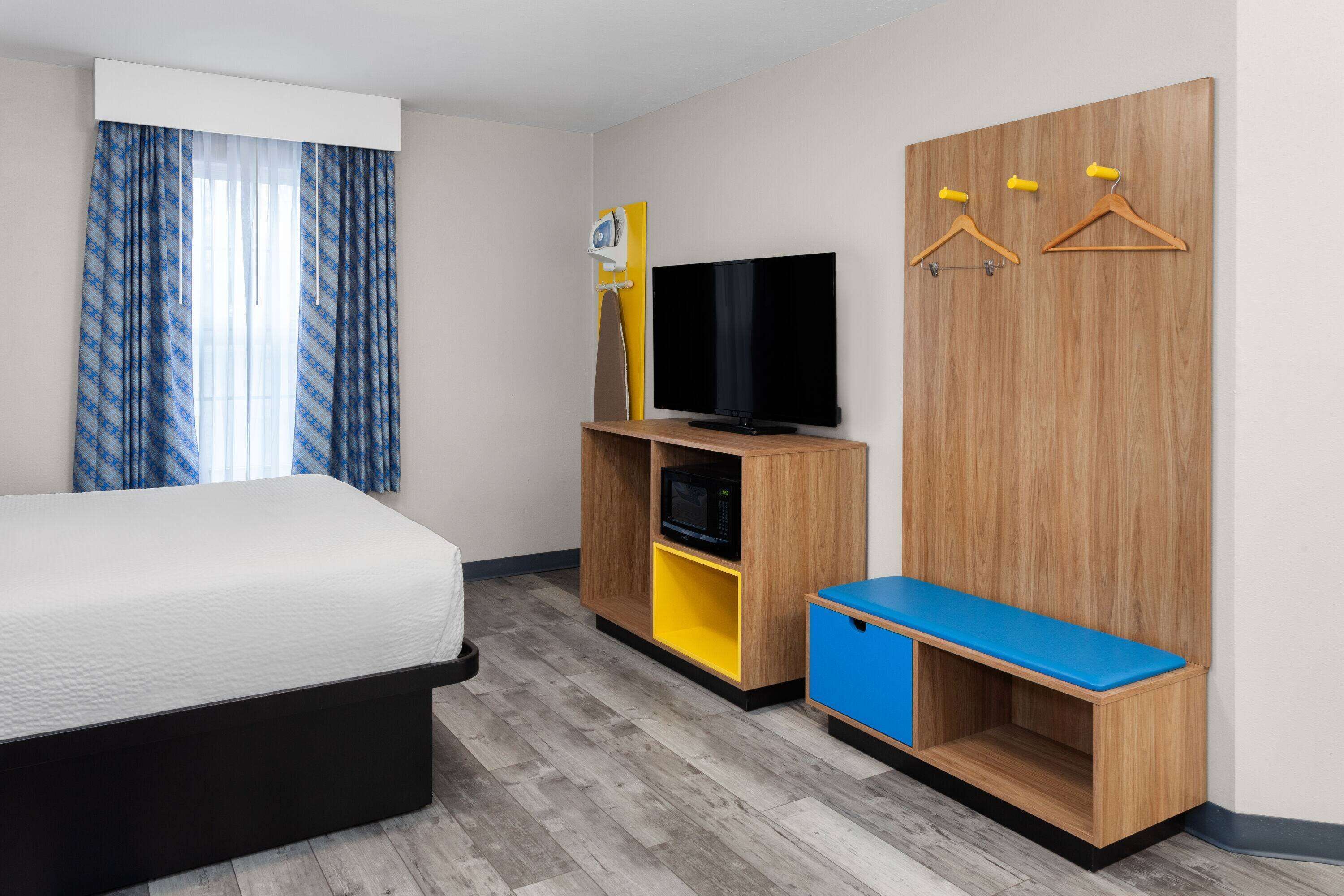 A hotel room with a bed, a TV, a wardrobe, and a bench.