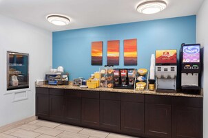 Una barra de desayuno con máquinas de café, un dispensador de café Folgers y una máquina dispensadora de crema Spray.