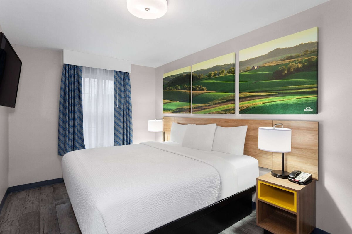 A hotel room with a large bed, a nightstand with a lamp, and a wall-mounted TV.