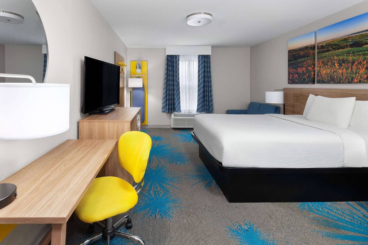 A hotel room with a bed, a desk, a chair, a television, and a window with curtains.