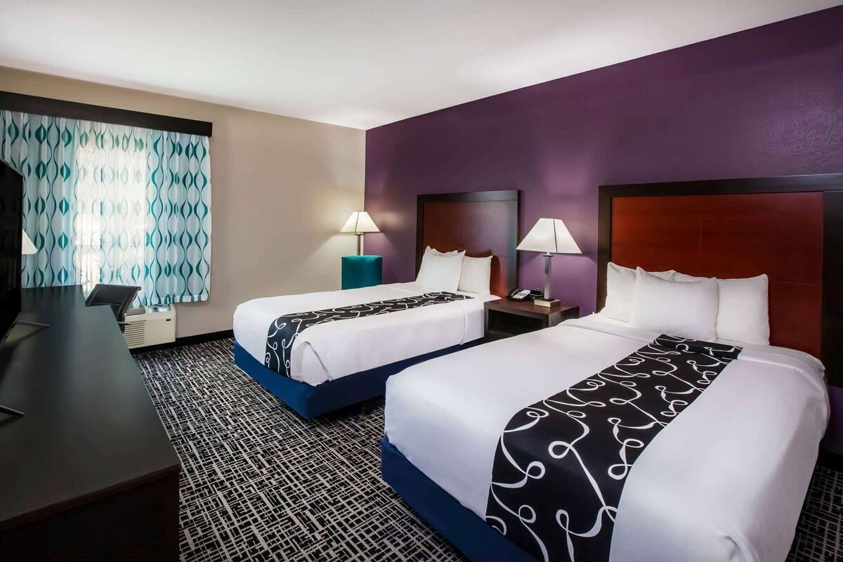 A hotel room with two beds, a desk, and a television.