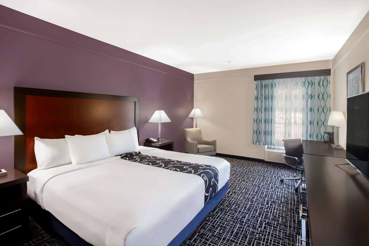 A hotel room with a large bed, two bedside tables with lamps, a desk with a TV, a chair, and a patterned carpet.