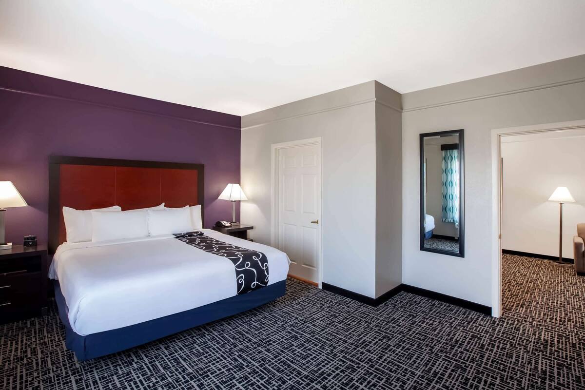 A hotel room with a large bed, two bedside tables with lamps, a door, and a mirror on the wall.