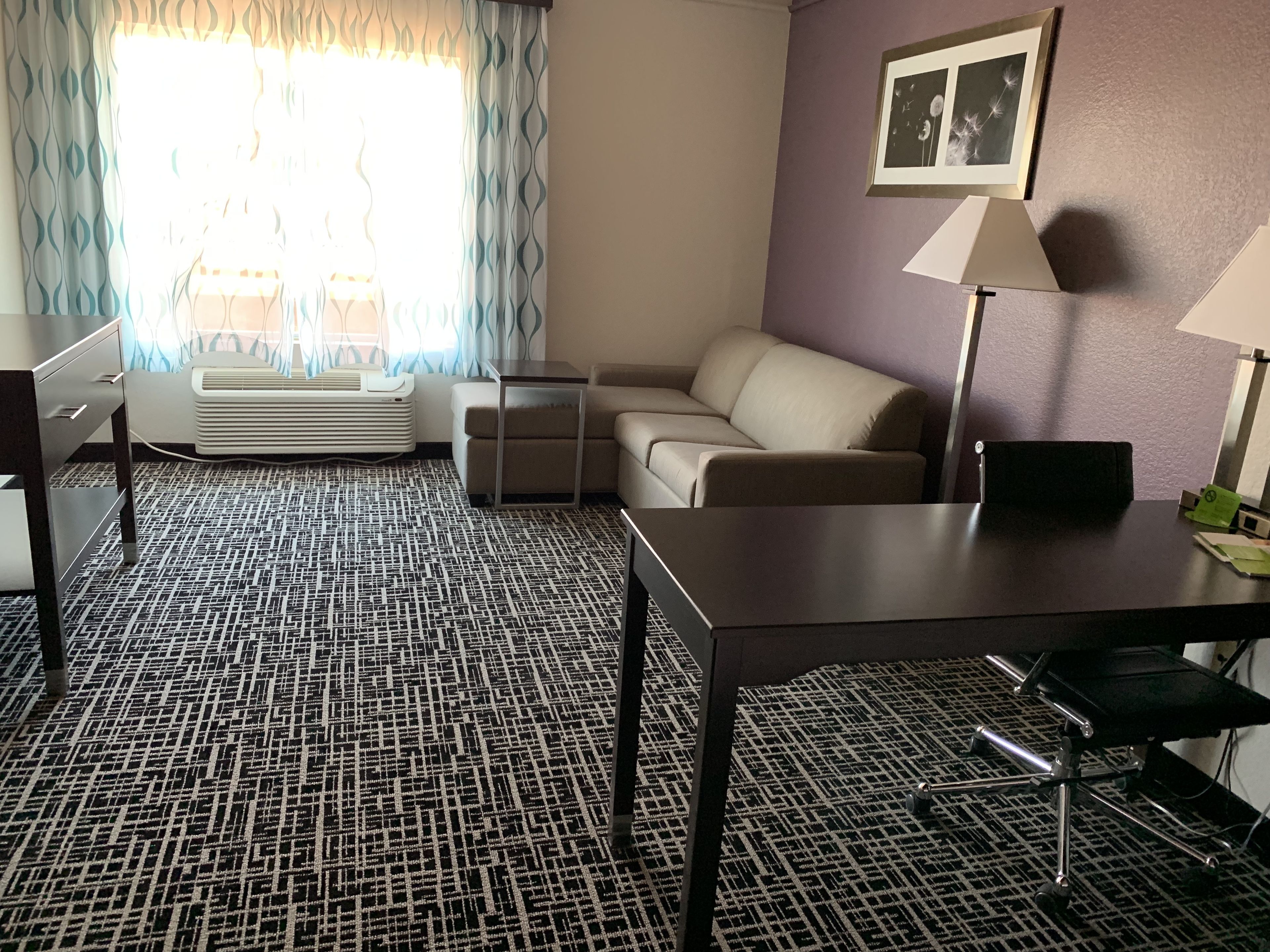 Een hotelkamer met een kamerbreed tapijt, een bank, een klein tafeltje, een bureau en een lamp.