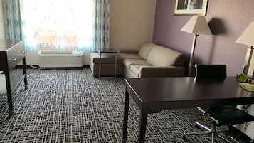 Een hotelkamer met een kamerbreed tapijt, een bank, een klein tafeltje, een bureau en een lamp.