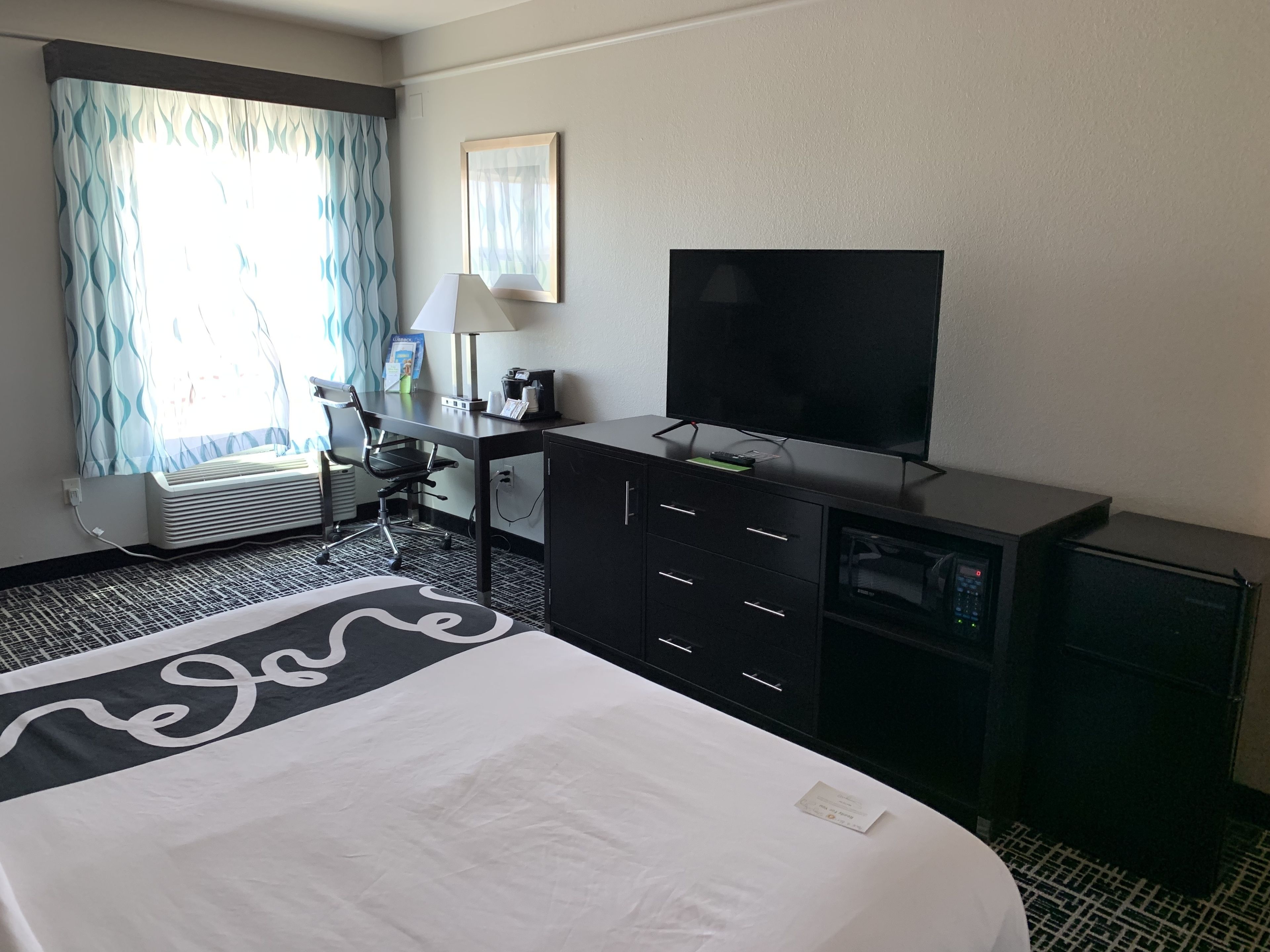 Ein Hotelzimmer mit einem Bett, einem Schreibtisch mit Fernseher, einem Sessel, einer Schreibtischlampe und einem kleinen Schrank.