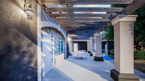 A covered outdoor corridor with a concrete floor, white doors, and a wooden pergola. - La Quinta Inn & Suites by Wyndham Lubbock North (Lubbock)