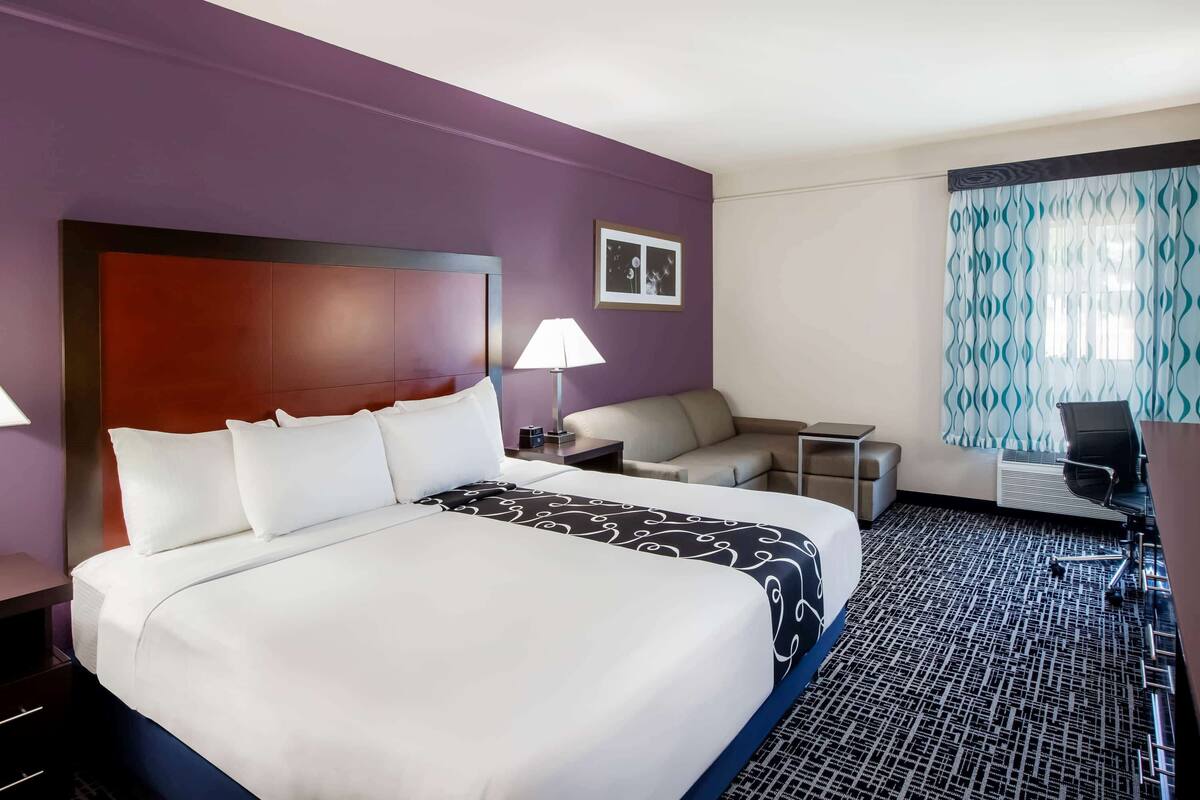 A hotel room with a large bed, a desk, a chair, a lamp, and a patterned curtain.