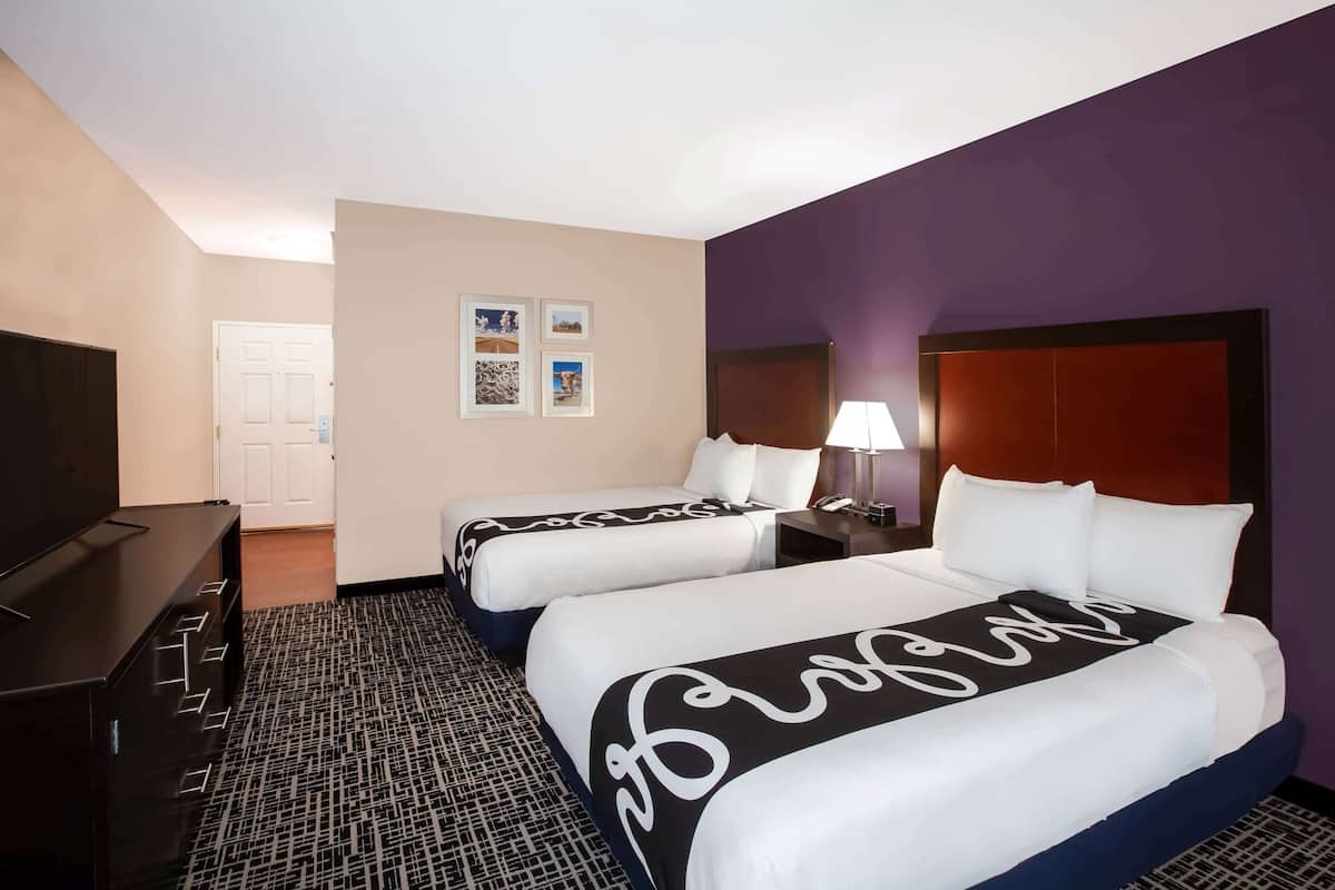 A hotel room with two beds, a TV, a desk, and a lamp.